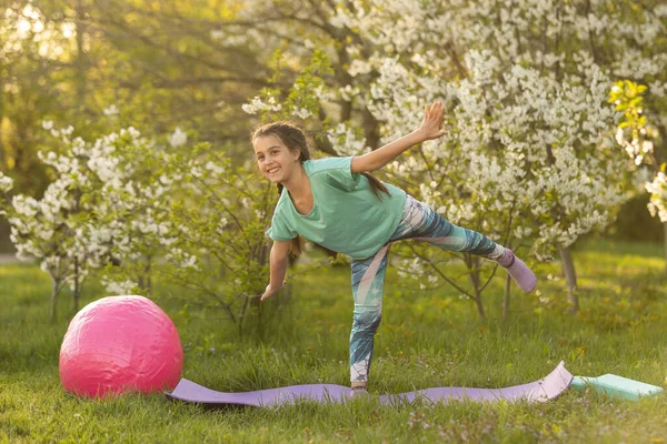 Niña haciendo ejercicio de yoga estirándose sobre la hierba en el soleado día de verano. Un niño flexible, haciendo ejercicios de gimnasia. Deportes, aprendizaje, fitness, estiramiento, yoga, conceptos de estilo de vida activo. —  Fotos de Stock
