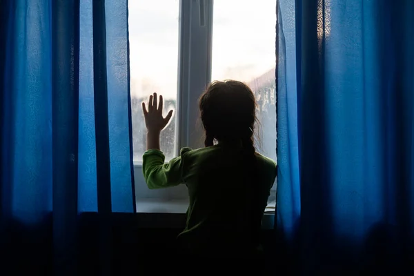 Child girls are standing in the dark, looking out the window, sad mood — Stock Photo, Image
