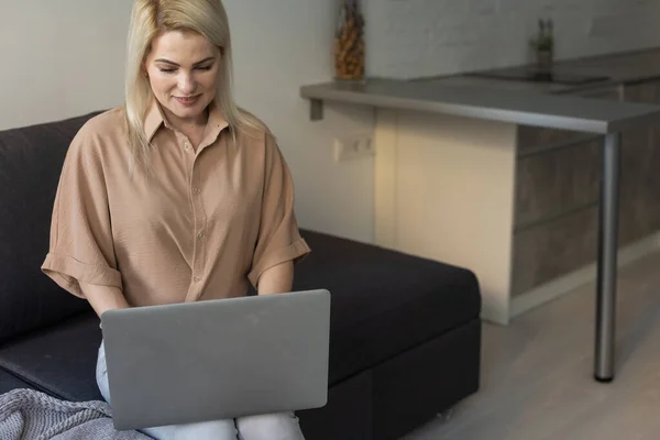 Sorrindo mulher feliz sentado no sofá e usando laptop. O conceito de trabalho remoto ou estudo durante a quarentena — Fotografia de Stock