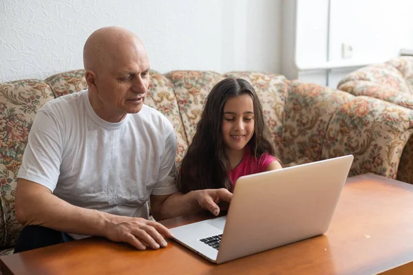 Adorabile bambina che abbraccia il nonno felice usando il computer portatile a casa . — Foto Stock