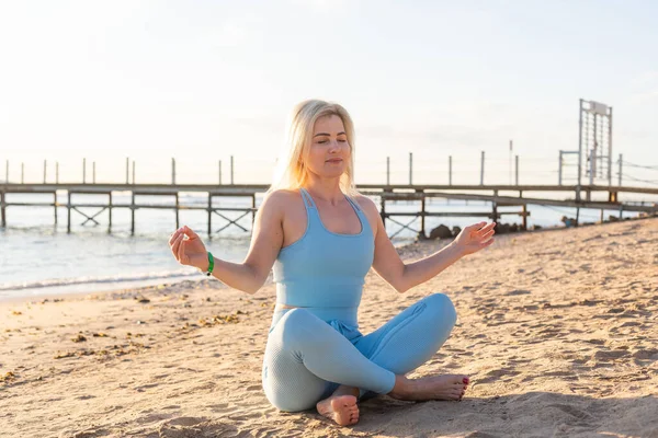 Attraente donna in forma che pratica affondi laterali, esercitandosi sulla spiaggia in una luminosa giornata di sole. Stile di vita sano, allenamento all'aperto — Foto Stock