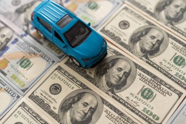 100 dolarlık banknotlarda küçük oyuncak araba, beyaz arka planda izole edilmiş yol olarak.