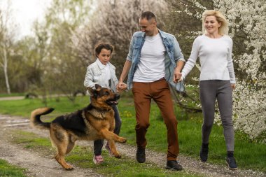 Mutlu genç aile dışarıda yeşil doğada birlikte vakit geçiriyor.