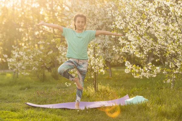 Красивая девушка делает упражнения йоги, маленькая девочка делает упражнения йоги в саду. — стоковое фото