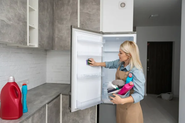 Jovem mulher limpeza geladeira com Rag em casa . — Fotografia de Stock