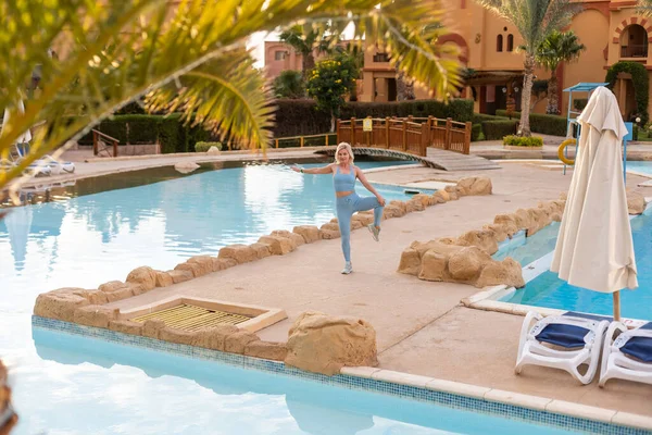 Foto al aire libre de la mujer joven en forma de sujetador deportivo de pie junto a la piscina. — Foto de Stock
