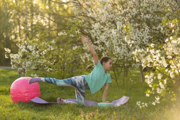 La ragazzina in maglietta fa yoga su un tappeto in giardino. un bambino e uno stile di vita sano — Foto Stock