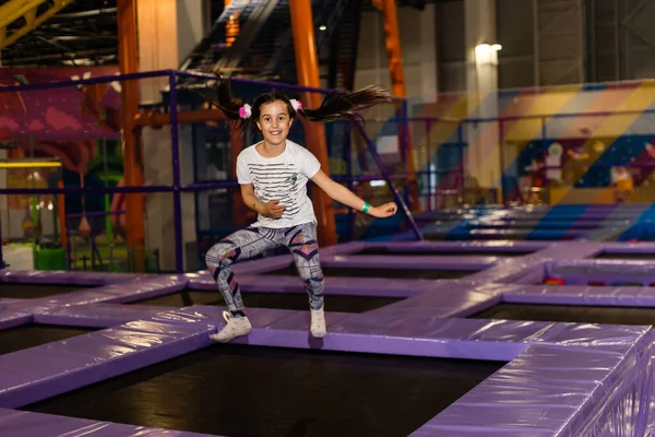 Çocukların oyun odasında, kapalı alanlarda oynayan ve trambolinde zıplayan küçük sevimli kız çocuğu portresi. Aktif kız spor merkezinde eğleniyor..