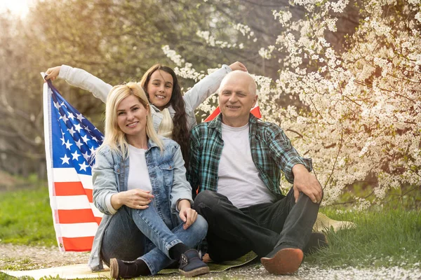 Patriotic family holding the usa flag outdoors. Happy aged caucasian couple holding the usa flag on the green background. — Stock Photo, Image