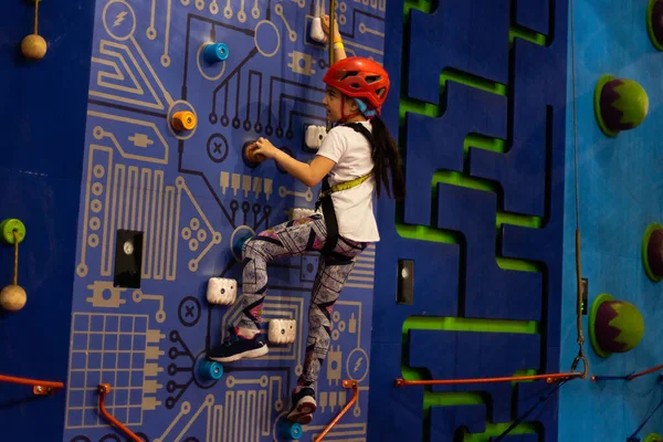 Hámos és biztonsági felszerelést viselő lány mászik a praktikus falon. Lány behelyezi a kötelet egy gyorshúzóba. — Stock Fotó