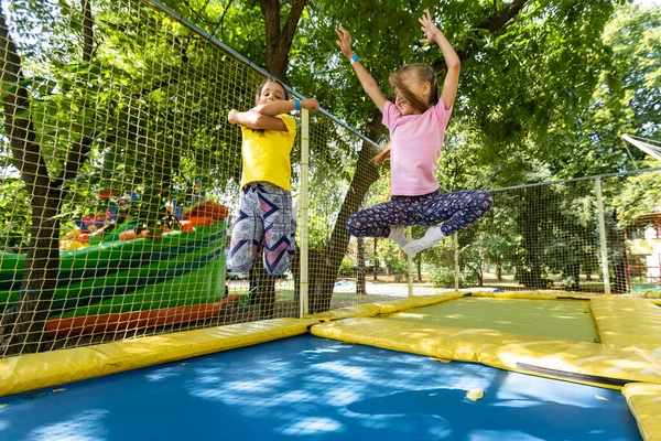 Little pretty girls having fun outdoor. Jumping on trampoline in children zone. Amusement park — Stock Photo, Image