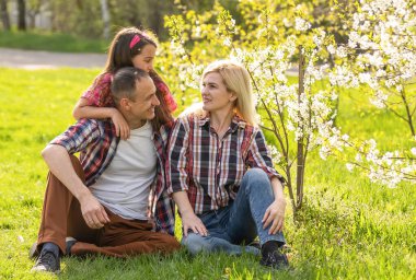 Mutlu ebeveynler anne, baba, kız, genç aile baharda açık havada çiçek açan elma ve kiraz ağaçlarının arka planında