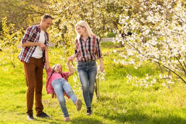 Mutlu genç aile dışarıda yeşil doğada birlikte vakit geçiriyor.