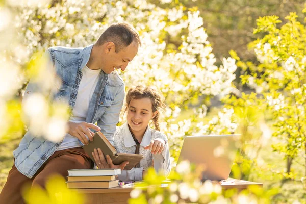 Caring young father helps little daughter, studying together watch online lesson on laptop, attentive dad and small girl child learning at home, have web class on computer on quarantine. outdoor — Stockfoto