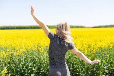 woman smiling in yellow rapeseed flowers on the field. Summer mood, happy vacation.