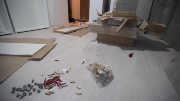 Parts of unfinished furniture, metal screws and tools lying on the floor with instruction manual for furniture assembly in the background. Moving to new home. — Vídeo de stock