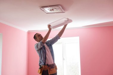 Elektrikçi tavana bir lamba yerleştiriyor..