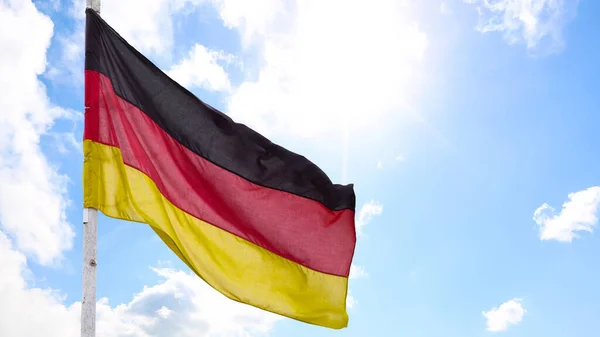 The official flag of Germany waving on a blue sky background. Horizontal banner design, with the German flag hanging on a sunny background with white clouds. Deutschland flag wide banner — стоковое фото