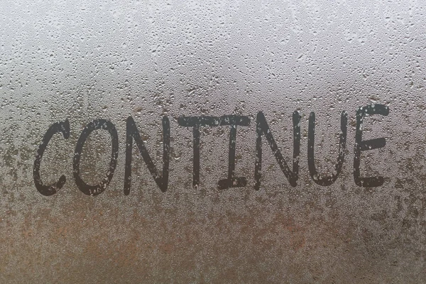 La palabra continuar escrito a mano en vidrio de ventana húmedo noche — Foto de Stock