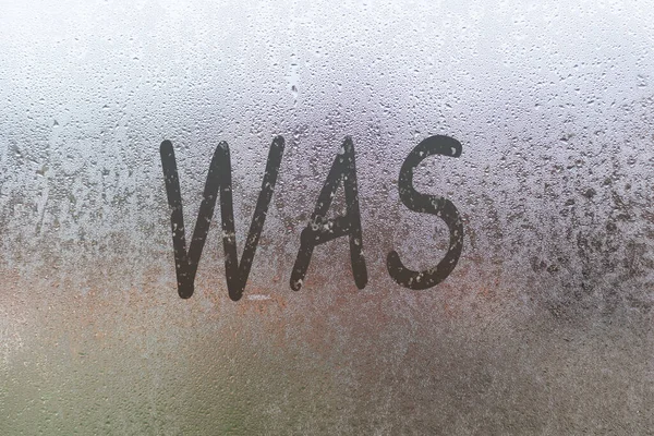 A palavra estava na janela enevoada. Condensação de gotas de água fundo de orvalho em vidro, umidade e nevoeiro vista de perto. — Fotografia de Stock