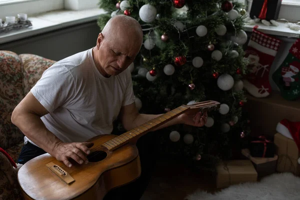 Conceito de família de pessoas felizes Velho homem sênior apreciando a guitarra no sofá da casa no Natal — Fotografia de Stock