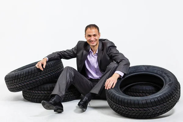 白い背景に隔離された車のタイヤの山にもたれている若いビジネスマンの完全な長さの肖像画 — ストック写真