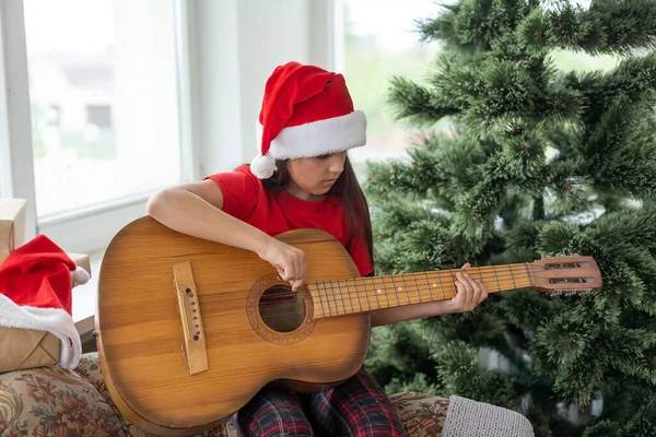 子供がギターを弾いてクリスマスツリーの近くで歌う — ストック写真