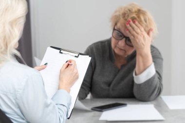 Kadın doktor olgun bir hastaya hastane ofisinde tedavi hakkında danışmanlık yapıyor, terapist ve üst düzey kadın sağlık ve kontrol sonuçlarını tartışıyorlar..