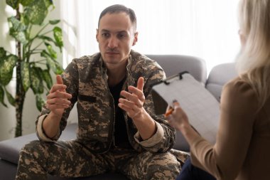 Psikolog, asker ve travma sonrası stres bozukluğu ile terapi seansında notlar alıyor..