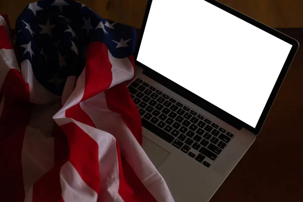 Laptop with blank screen and USA flag on desk in office.