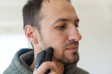 Yakışıklı genç adam gri arka plan üzerinde elektrikli ustura ile tıraş