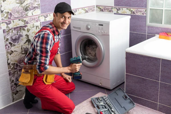 working man plumber repairs a washing machine in laundry