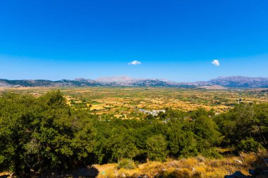 Kretes Denizi ve dağ bitkileriyle dolu kayalar. Mavi gökyüzü, harika bir manzara. Temiz su ve dağlar