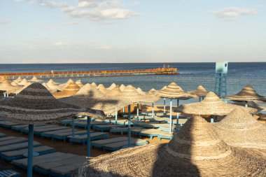 Kumsalda güneşli yatakları ve saman güneş şemsiyeleri olan Akdeniz kıyıları.