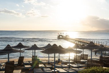 Kumsalda güneşli yatakları ve saman güneş şemsiyeleri olan Akdeniz kıyıları.