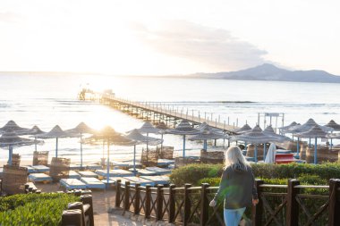 Plajda gün batımında palmiye ağaçları, şemsiyeler ve güneş yatakları. Aile Tatilleri Denizde