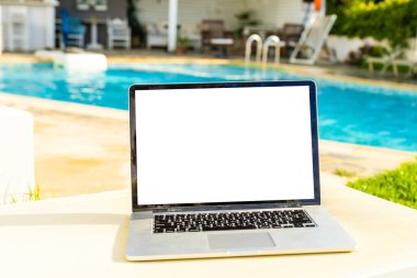 Güneşli bir havada, güzel bir ev bahçesinin avlusunda boş ekranlı bir dizüstü bilgisayar duruyor.