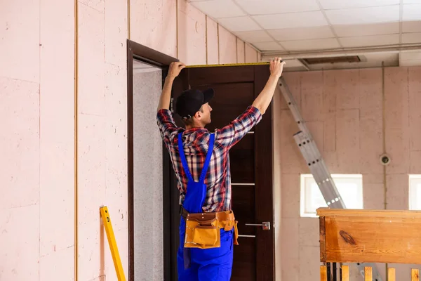 Carpenter worker installation process of measures cloth with ruler door hinge.