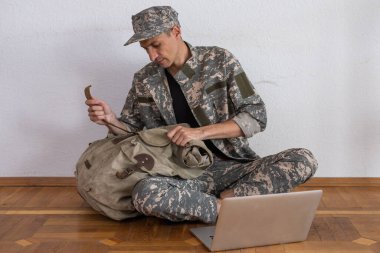 Donanma üniformalı gülümseyen genç adam beyaz arka planda dizüstü bilgisayar tutuyor.