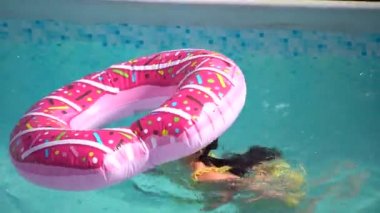 Bir donut şişme daire üzerinde yatan bir mayo içinde sevimli küçük kız. Çocuk mavi bir arka plan üzerinde yüzer.