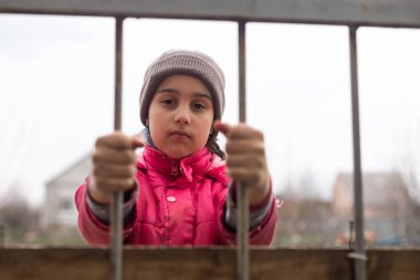 Parmaklık tutan küçük bir kızın fotoğrafı. Demir parmaklıklar arkasında üzgün küçük bir kız. Parmaklıkların arkasındaki küçük kız. Şiddet kavramı