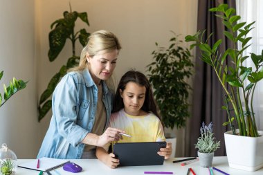 Çekici küçük kız ve güzel genç annesi dijital tablet kullanıyorlar ve evde gülümsüyorlar..