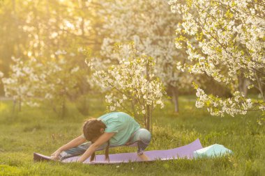 Küçük bir kız parkta bir spor minderinin üzerinde yoga yapıyor. Sağlıklı bir yaşam tarzı çocukça bir alışkanlıktır..