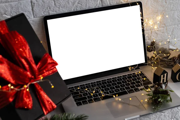 Front view of the laptop with mockup screen on the desk. Christmas gifts and decorations behind laptop. Holiday online shopping or sale. Internet goods. Copy space. Reindeer, Christmas tree