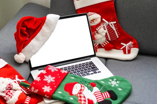 Laptop with blank screen on a desktop at home, Christmas gifts and decorations in the background.