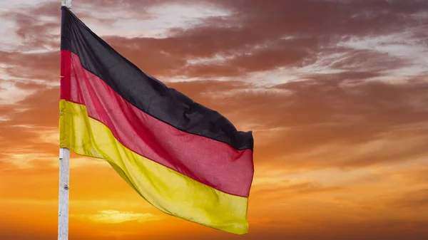 The official flag of Germany waving on a blue sky background. Horizontal banner design, with the German flag hanging on a sunny background with white clouds. Deutschland flag wide banner.