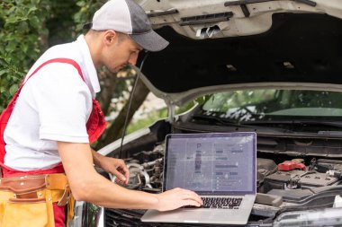 Makinist araba motoru yakınındaki dizüstü bilgisayar ile. Modern araba tanılama programı üstünde perde. Araba hizmet anlayışı.