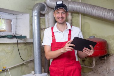 Teknisyen elinde tabletle kazan dairesindeki ısıtma sistemini kontrol ediyor.