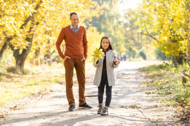 Küçük kızıyla mutlu, genç bir baba. Baba ve küçük çocuk dışarıda eğleniyor, sonbahar parkında birlikte oynuyorlar. Babası çocuğuyla gülüyor ve doğanın tadını çıkarıyor..