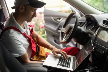 Tamirci, dizüstü bilgisayarı kullanarak kapatıyor. Akort onarımı, araba motoru otomobil parçalarını tamir ediyor. Atölye garajı destek servisindeki aletleri genel iş üniformasında kullanıyor..